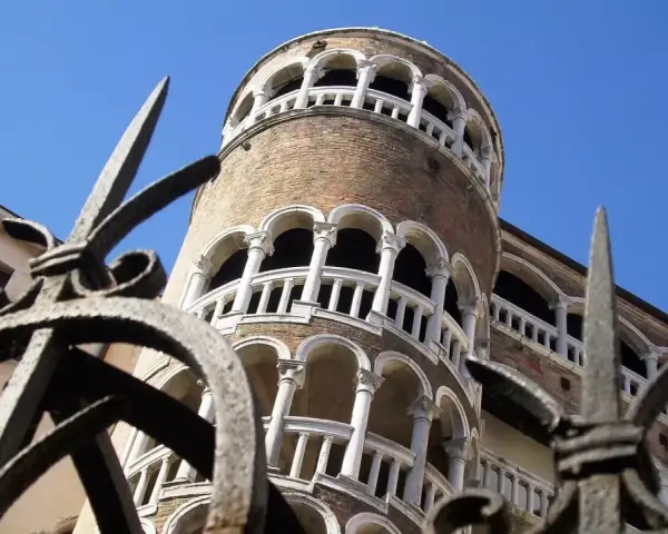 La Torre del Bovolo, con la sua architettura a chiocciola e i suoi loggiati, si staglia contro il cielo azzurro, vista attraverso un cancello in ferro battuto.