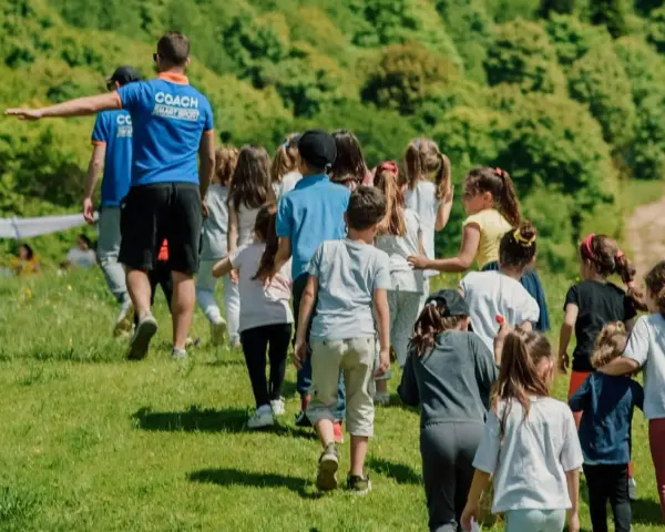 Un groupe d'enfants suit un coach sur une colline verdoyante. Ces actions pour financer un voyage scolaire sont pleines d'énergie et de joie.
