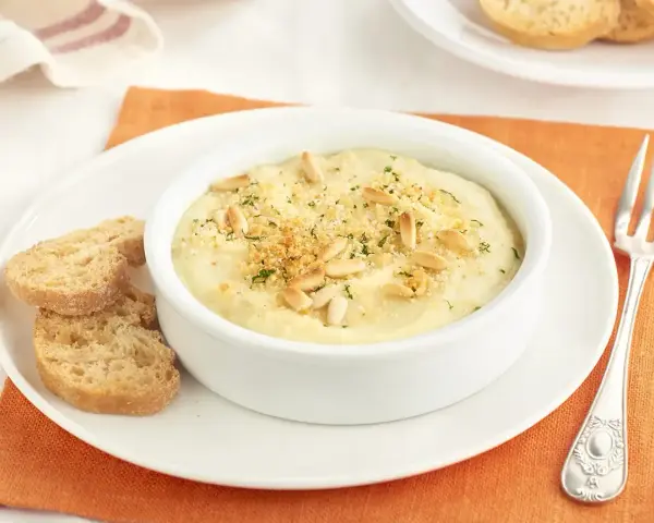 Deliciosa brandada de merluza cremosa, gratinada con piñones y pan rallado, servida con tostas.