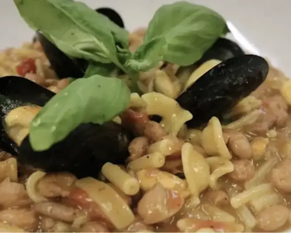 Un piatto invitante di pasta fagioli e cozze, guarnito con foglie di basilico fresco.