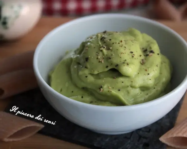 Una ciotola bianca piena di vellutata crema di avocado, cosparsa di pepe nero macinato. Accanto, pasta integrale.