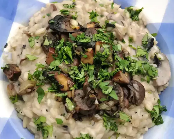 Risotto cremoso con champiñones salteados y perejil picado en un plato azul a cuadros.