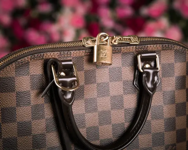 Dettaglio di una borsa Louis Vuitton, icona dell'azienda, con il classico motivo a scacchiera e un lucchetto dorato.