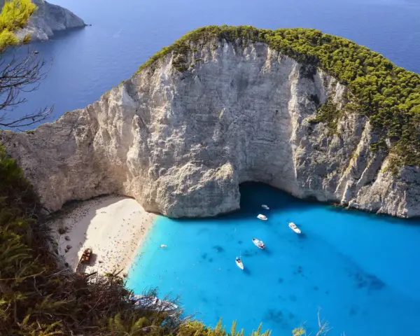 Widok na zatokę Navagio na Zakynthos z plażą, turkusową wodą i łodziami.