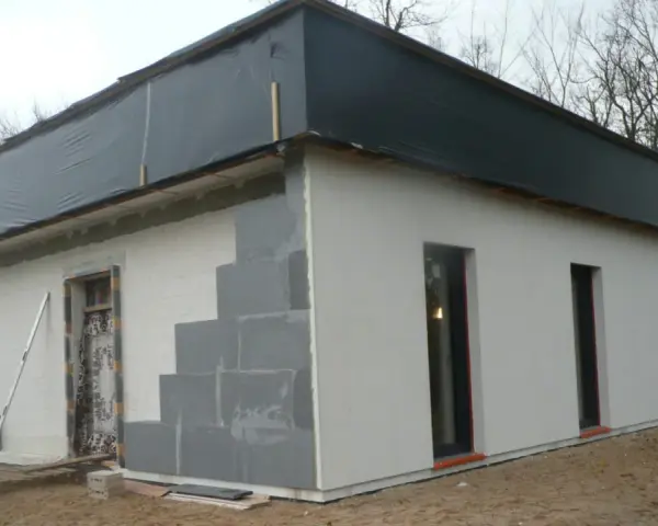 Budowa domu ze styropianu w trakcie. Widoczne bloczki, okna i dach przykryty czarną folią.