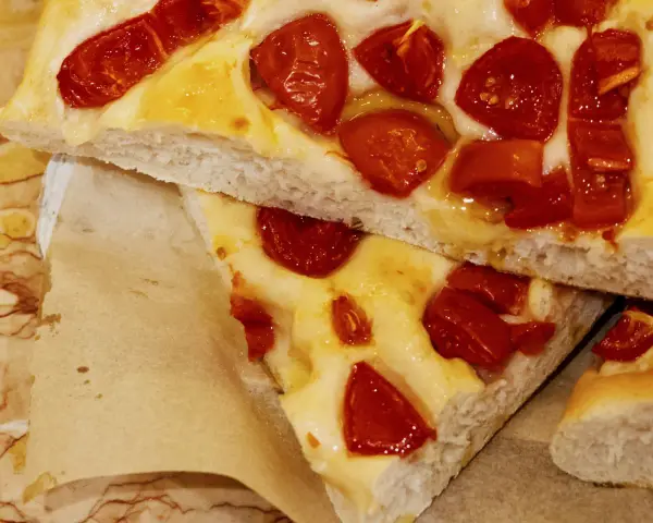 Saftige Focaccia Pomodoro mit geschmolzenem Käse und sonnengetrockneten Tomaten, auf Backpapier serviert.