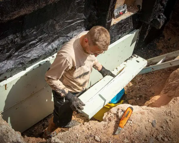 Mann verlegt Dämmplatten für die Kellerabdichtung. Das ist ein wichtiger Schritt, um später Drainage zu verlegen und das Mauerwerk trocken zu halten.