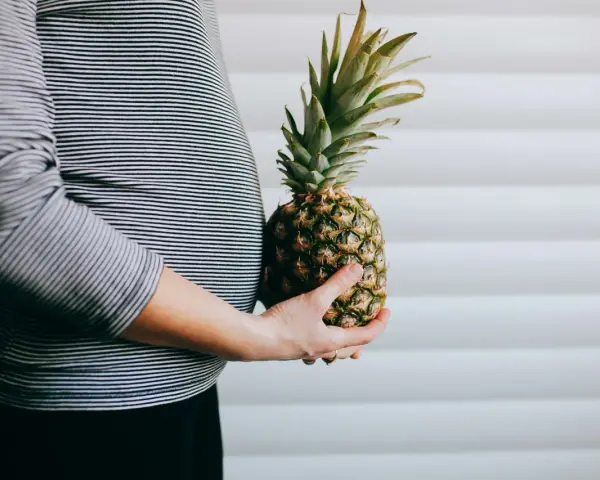 Brzuch kobiety w paski, trzymająca ananasa. Wygląda jak ananas w ciąży, symbolizujący zdrową dietę.