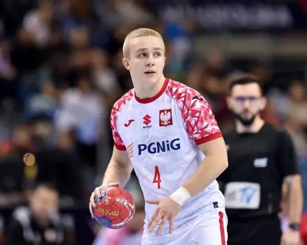 Młody zawodnik w białej koszulce z orłem i numerem 4, gotowy do rzutu piłką ręczną.
