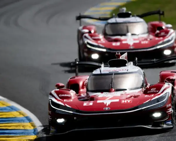 Dos coches de carreras rojos compiten en Le Mans, sus luces brillan en la pista.