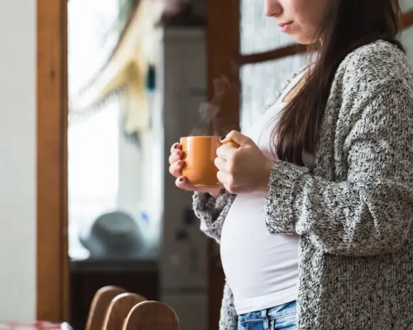 Ciepły napar z rooibos w dłoniach ciężarnej kobiety. Delikatny dym unosi się z kubka, tworząc chwilę spokoju.