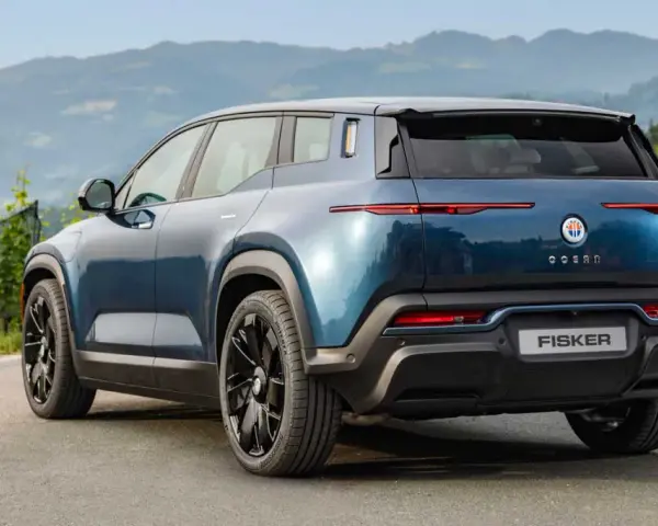 Tylna część niebieskiego elektrycznego SUV-a Fisker Ocean na tle gór i zieleni.