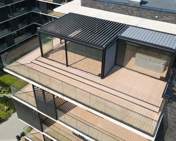 Nowoczesny taras na dachu z przeszklonym pawilonem i pergolą. Drewniana podłoga i szklane balustrady tworzą elegancką przestrzeń.