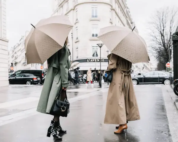 Dos mujeres con paraguas lucen elegantes gabardinas, como se llaman las chaquetas largas, en un día lluvioso en París.