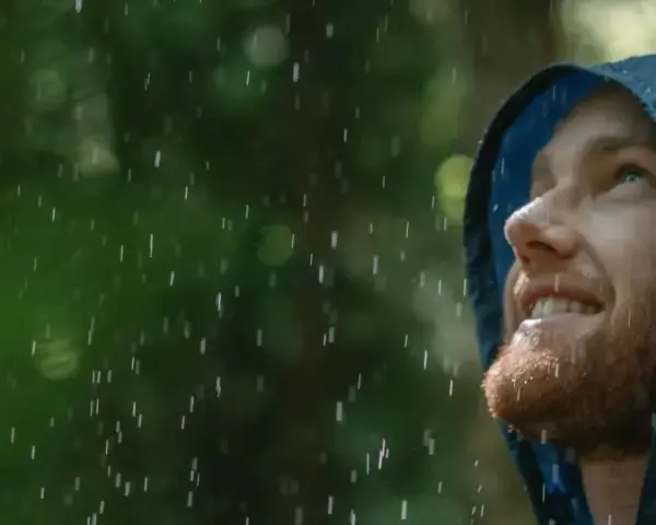 Mann mit Bart blickt lächelnd in den Regen, seine blaue Regenjacke hält ihn trocken.