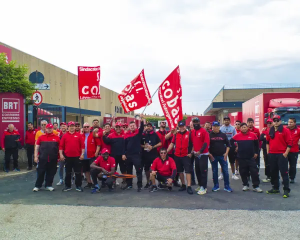 Un gruppo di lavoratori BRT, con bandiere rosse, manifesta per migliorare le condizioni di lavoro. Le loro opinioni su lavorare in Bartolini sono chiare.