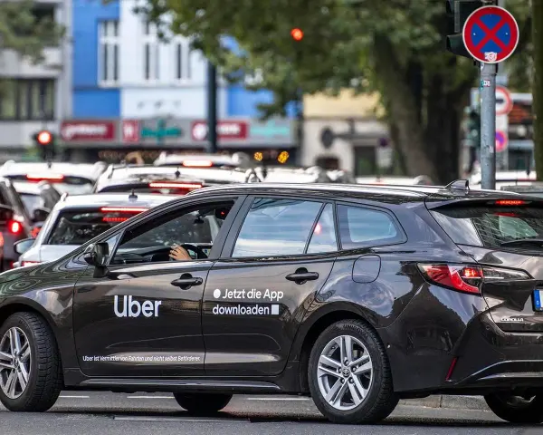 Ein dunkler Uber-Kombi steht im Stau. Die Aufforderung "Jetzt die App downloaden" ist gut sichtbar.