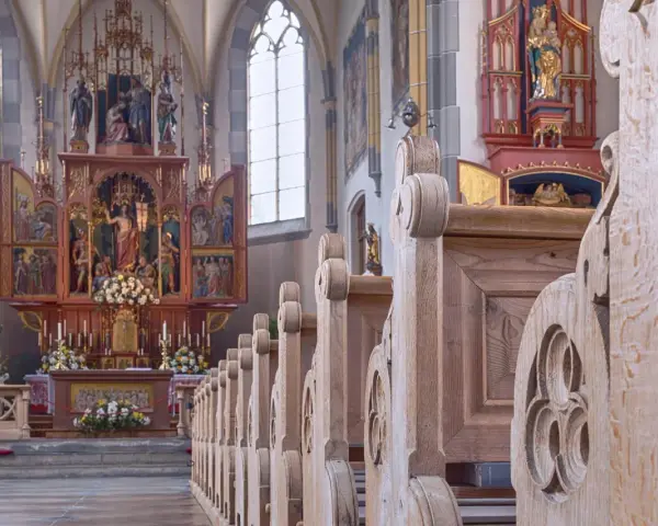 Drewniane ławki w kościele św. Jana w Warszawie, prowadzące do ołtarza z bogatymi zdobieniami i figurami.