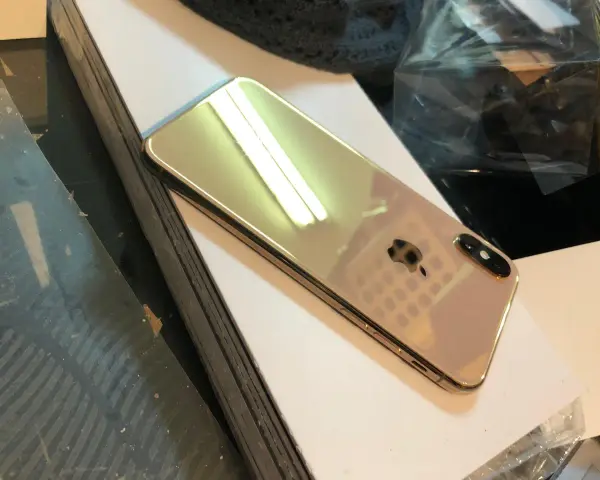 Błyszczący, złoty iPhone X leży na białej powierzchni.