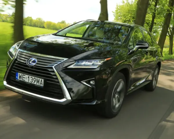 Czarny Lexus RX 450h pędzi po wiejskiej drodze, otoczony zielenią drzew i pól.