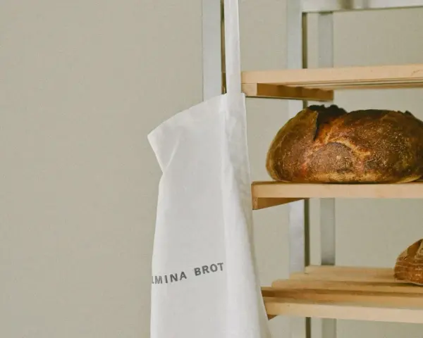 Ein weißer Stoffbeutel mit der Aufschrift "WILMINA BROT" hängt neben einem Regal mit frisch gebackenen Broten.