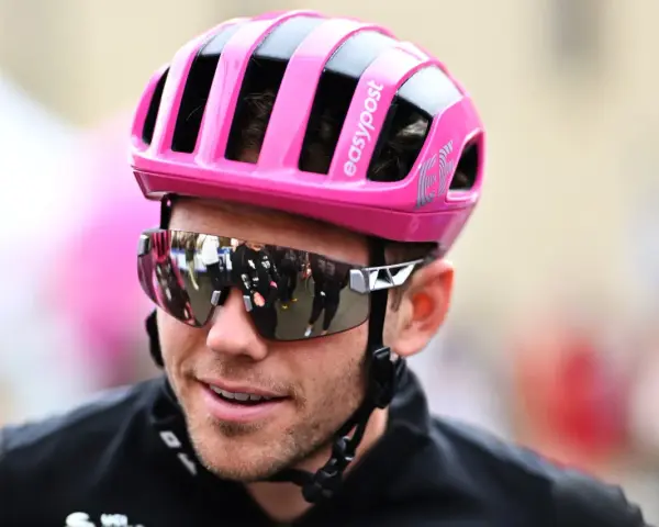 Cyclist Luke Lamperti smiles, wearing a bright pink helmet and reflective sunglasses.