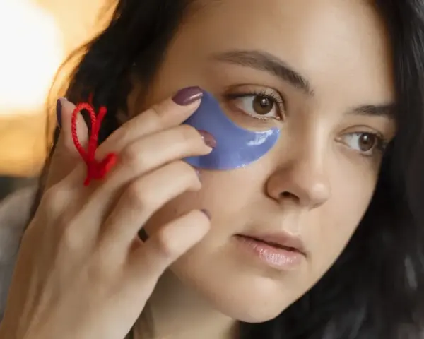 Una mujer se aplica parches de ojos morados. Muestra cómo se ponen los parches de ojos para un cuidado facial.