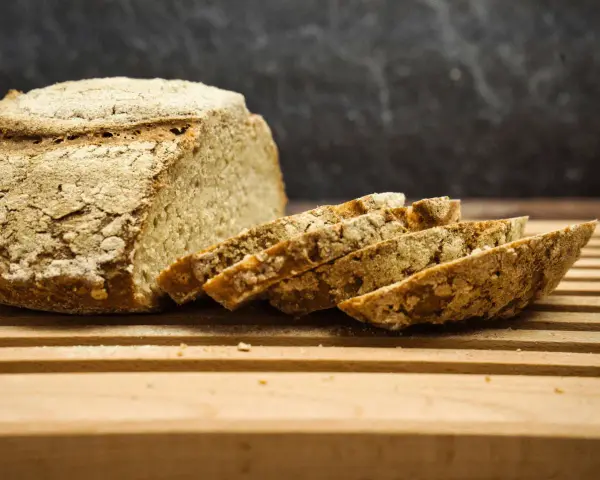 Ein rustikales, selbstgebackenes Brot liegt angeschnitten auf einem Holzbrett. Die Kruste ist knusprig, die Scheiben duften nach Tradition.