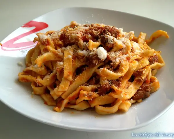 Un piatto invitante di tagliatelle al ragù, condite con abbondante parmigiano grattugiato.