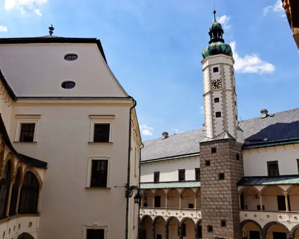 Dziedziniec zamku w Bruntalu, Czechy. Białe mury, arkadowe krużganki i wysoka wieża zegarowa pod błękitnym niebem.