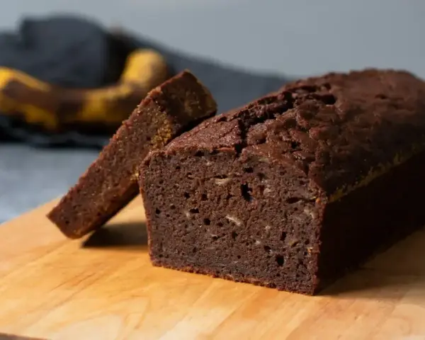 En saftig banankaka i långpanna, med en skiva uppskuren. En övermogen banan ligger i bakgrunden, redo att bli en del av nästa bakverk.