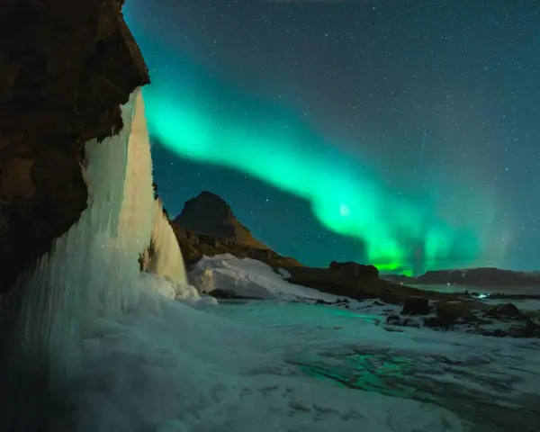 Lodowy wodospad i zorza polarna na nocnym niebie. Islandia w styczniu, magiczny widok.