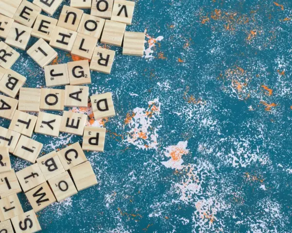 Fichas de letras de madera esparcidas, algunas formando palabras con w, sobre un fondo azul texturizado con salpicaduras blancas y naranjas.