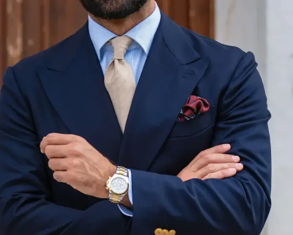 Uomo con abito blu, cravatta beige e fazzoletto bordeaux con un disegno floreale. Il fazzoletto, un dettaglio di stile, aggiunge un tocco di eleganza.