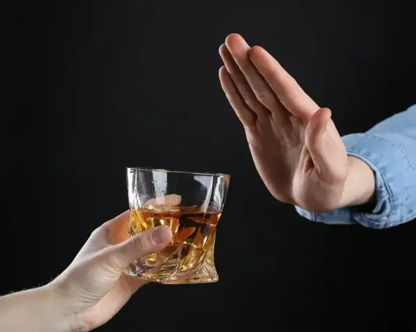 Ręka odrzuca szklankę z bursztynowym płynem. Czy dzień przed wizytą u dentysty można pić alkohol? Lepiej unikać.