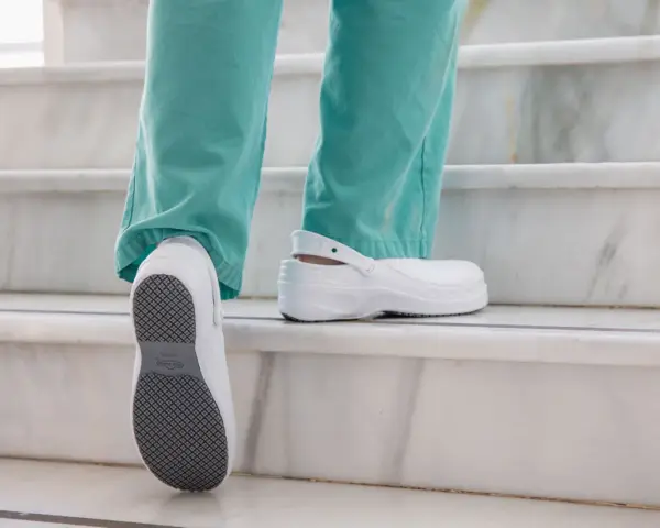 Persona subiendo escaleras con zapatos blancos, mostrando la suela antideslizante. El poliuretano en zapatos ofrece comodidad y durabilidad.