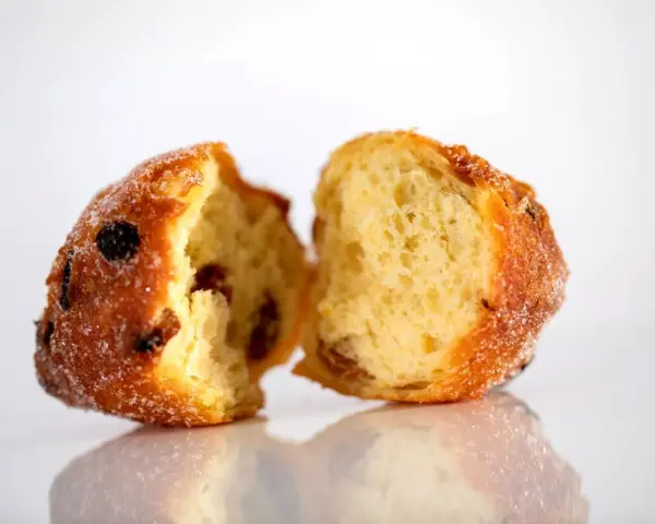 Frittelle veneziane, dolci e soffici, con uvetta e zucchero, spezzate a metà per mostrare l'interno invitante.