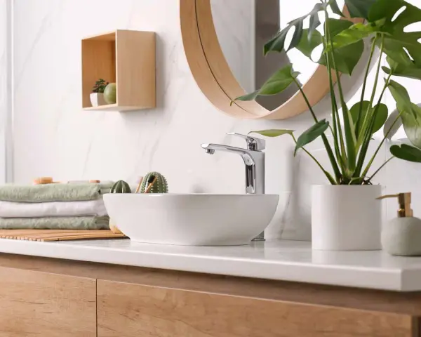 Plan de travail de salle de bain moderne avec vasque, robinetterie chromée, serviettes pliées et plante verte. La hauteur du plan de travail est idéale.