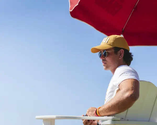 Ein Rettungsschwimmer mit gelber Kappe und Sonnenbrille wacht am Pool des **summer camp**.