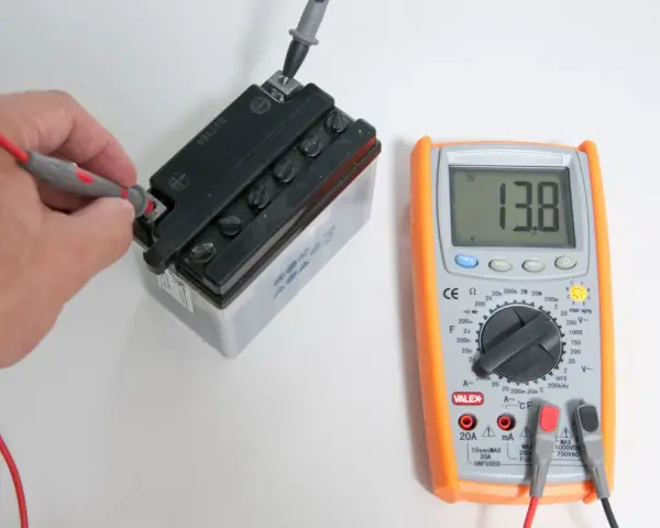 Una mano usa il multimetro per misurare la tensione di una batteria, mostrando 13.8V.