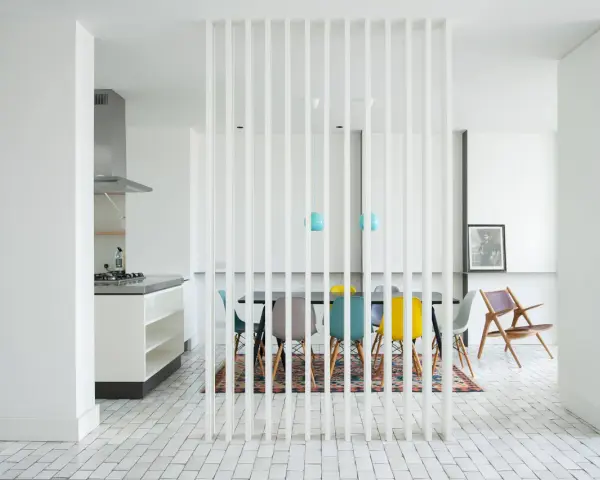 Elegante solución para dividir salón en dos ambientes. Cocina moderna y comedor con sillas de colores, separados por una celosía blanca.