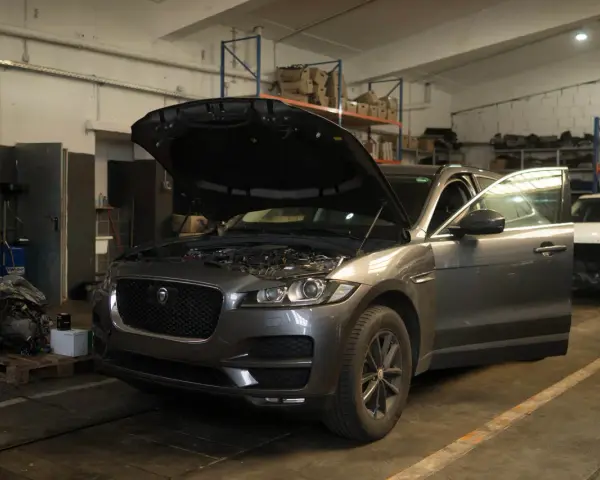 Grauer Jaguar XE mit geöffneter Motorhaube und Tür in einer Werkstatt, bereit für Reparaturen wegen Jaguar XE Probleme.