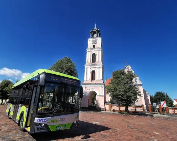 Zielony autobus MZK Chodzież czeka na pasażerów pod wieżą kościoła. Sprawdź mzk chodzież rozkład jazdy i zaplanuj podróż!