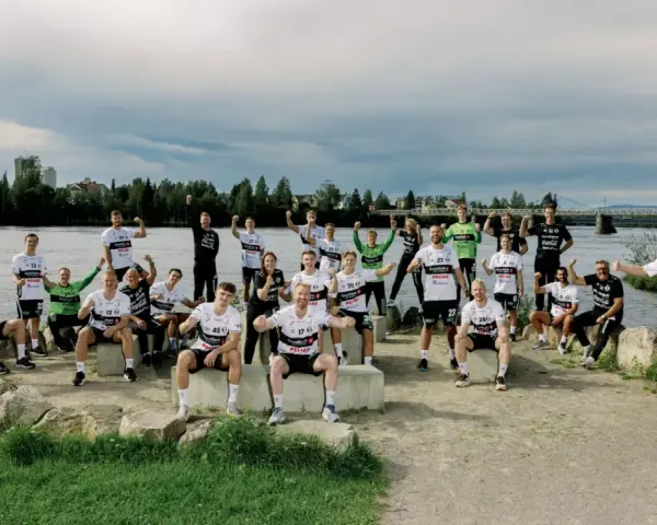 Drużyna Elverum Handball świętuje nad rzeką, pozując do wspólnego zdjęcia w sportowych strojach.