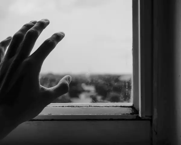 Dłoń oparta o brudną szybę, symbolizująca strach przed ludźmi i izolację od świata zewnętrznego.