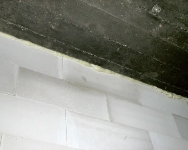 Piana montażowa wypełnia szczelinę między betonowym stropem a białą ścianą z bloczków, tworząc dylatację.
