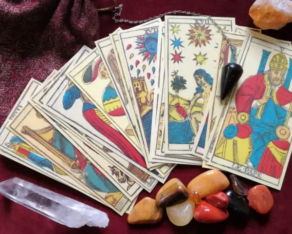 Cartas de tarot psicológico, un péndulo y cristales dispuestos sobre una tela burdeos.