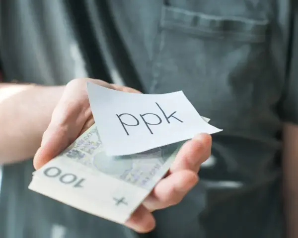 Dłoń trzyma banknoty i karteczkę z napisem "ppk". Jak sprawdzić swoje oszczędności?