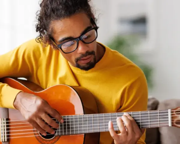 Mann mit Brille hält eine Gitarre und spielt darauf.