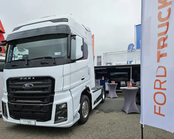 Biały Ford F-MAX prezentuje się na wystawie, obok banerów z logo Ford Trucks.